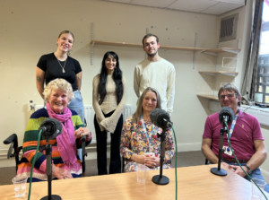 BCU students Maya Davis and Kyle Salmon with lecturer Meera Darji, and podcast guests Joan Fairley, Rachel Barker and Andy Barker at the microphone during podcast recording at St Giles Hospice